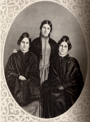 A black and white photograph of the Fox sisters, Leah, Margaret, and Kate, three young women in Victorian-era clothing, seated around a table.